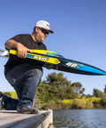 Person holding Sonicwake RC Boat 48 Inch Self Righting Brushless 8S Ready To Run with Spektrum electronics by lake.