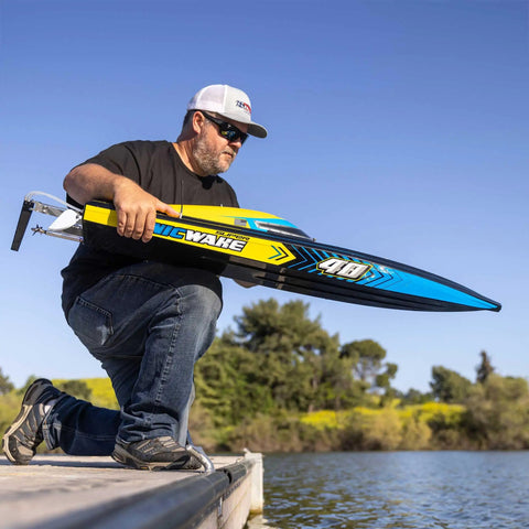 Person holding Sonicwake RC Boat 48 Inch Self Righting Brushless 8S Ready To Run with Spektrum electronics by lake.