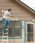 A person using a mobile airless paint sprayer on home siding while standing on a ladder for Crush Huge Painting Jobs Straight Up With Heavy Duty Mobile Airless Paint And Stain Sprayer Cart For Butter Smooth Finishes On Home Exteriors Sheds And Fence Panels.