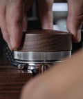 Close-up of hand using Walnut 58.35mm Espresso Distribution Tool, Adjustable Depth, Stainless Steel Leveler For 58mm Portafilters.