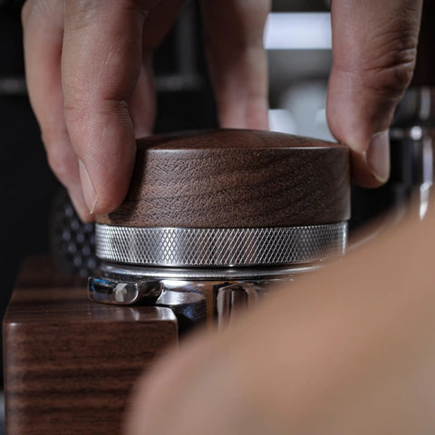 Close-up of hand using Walnut 58.35mm Espresso Distribution Tool, Adjustable Depth, Stainless Steel Leveler For 58mm Portafilters.