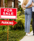 Couple standing near a 'For Sale' and 'Parking' sign in a garden setting.