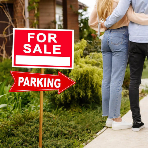 Couple standing near a 'For Sale' and 'Parking' sign in a garden setting.