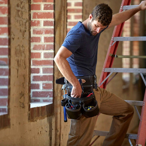 Worker wearing durable oil tanned leather tool rig with large capacity for hand tools and fasteners on a construction site ladder