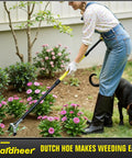 Person using Long Reach 4-In-1 Garden Hoe With 64 Inch Handle for easy weeding in flower beds, accompanied by a dog.