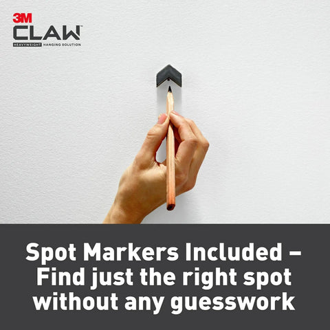 Hand holding pencil against wall using Claw 65 Lb Drywall Picture Hangers With Spot Markers No Studs Needed 3 Pack Heavy Duty Hangers.