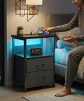 LED Nightstand With Charging Station, USB Ports And Outlets, Dope RGB Color Changing LED Night Light, Built In Storage Drawers, Space Saving Bedside Table For Small Rooms, Modern Black Finish, showing a phone being charged and digital clock in dim room lighting.