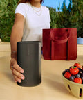 Person placing Take Anywhere Portable Bluetooth Speaker With WiFi Alexa Built In 24 Hour Battery Life on outdoor table