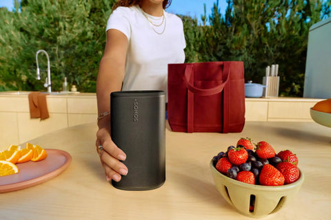 Person placing Take Anywhere Portable Bluetooth Speaker With WiFi Alexa Built In 24 Hour Battery Life on outdoor table