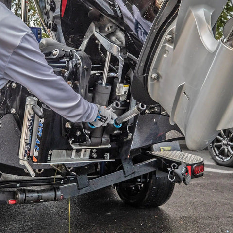 Person installing Motor Stik Pair Heavy Duty 8.75 Inch Transom Saver on outboard motor for trailering on wet pavement.