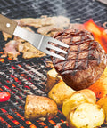 4 Piece Stainless Steel BBQ Grill Utensil Set With Wood Handles meat fork holding steak over grill with vegetables