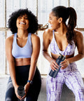 Two women in athletic wear holding a 24oz Insulated Water Bottle Built Tough With Premium Stainless Steel And Double Wall Vacuum Keeping Drinks Icy Cold Through Any Adventure Featuring Chug Ready Leakproof Straw And Wide Mouth Lids For The Daily Grind Or Trail Hikes In Smooth Black.