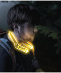 Person wearing rechargeable LED neck light, illuminating path in dark forest, showing hands free work light for mechanics campers hunters and DIY fans rugged water resistant neck light with nine hours runtime per charge USB cable included and four brightness modes for reading and projects.