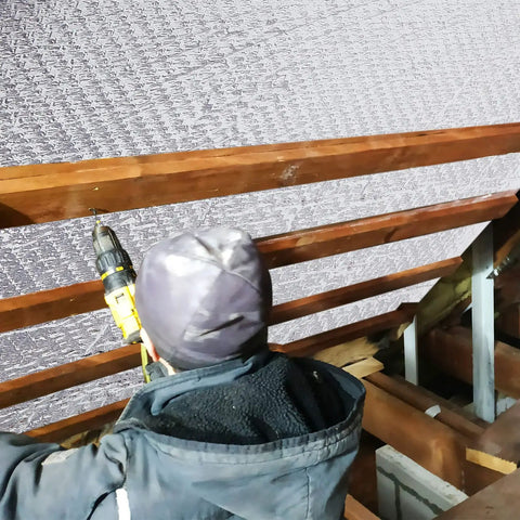 Person installing Double Bubble Reflective Foil Insulation Roll 16.5 Inch Wide By 15 Feet Long Aluminum Foam in attic rafters