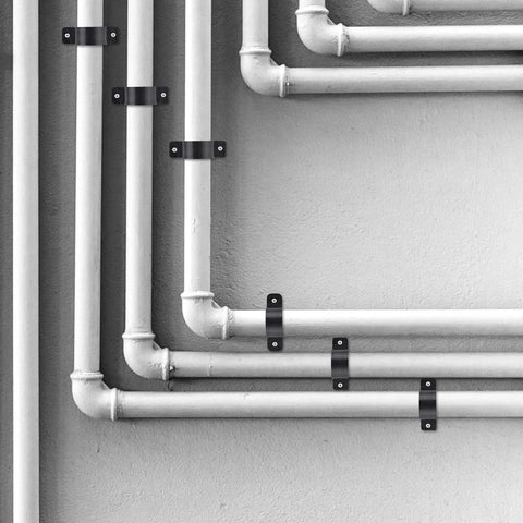Front view of black metal pipe support clamps securing white PVC/PEX pipes to a wall; several clamps visible.