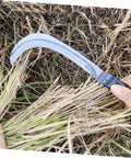 Two Pack Manganese Weeding Sickle Tool Set Durable Handheld Cutter For Efficient Harvesting And Gardening With Comfortable Non Slip Grip Great For One Handed Use In Weeding And Cultivating Your Yard And Beds. Close-up of sickle cutting grass with wooden handle.