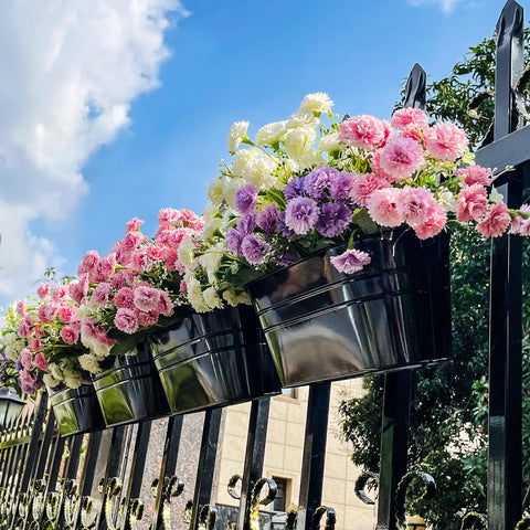 Four Pack Hanging Flower Pots, Metal Iron Wall Planter For Indoor And Outdoor Use On Railing, Fence, Balcony Or Garden, With Detachable Hooks And Drainage Holes. Flower-filled metal planters hung on a fence.