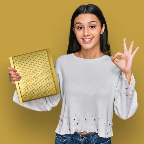 Smiling woman holding a Gold Bubble Mailers 6x10 For Jewelry And Makeup Supplies 50 Pack Metallic Envelope against a gold background.