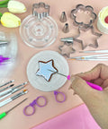 Badass 112 Piece Baking Decorating Kit With Sturdy Acrylic Turntable, Flexible Silicone Piping Bags, Precision Nozzles, Icing Bottles, And Surefire Gear For Sweet Cookies And Cupcakes - Star-shaped cookie being decorated.