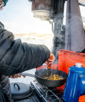 Person cooking with Percolator Coffee Pot For Campfire Brewing, Enamel Camping Kettle For Outdoors next to pan on camp stove.