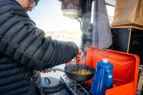 Person cooking with Percolator Coffee Pot For Campfire Brewing, Enamel Camping Kettle For Outdoors next to pan on camp stove.