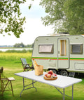 6 Foot Folding Table Portable Beefy Heavy Duty Plastic Fold In Half Utility Table For Indoor Outdoor Use Perfect For Camping Picnics Parties And Event Setups White in outdoor camping scene with a caravan and greenery.