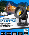 Lit 20W Outdoor COB Landscape Spotlight With Dusk To Dawn Sensor, black housing, warm light, in front of a house at dusk.