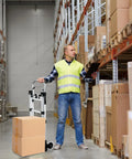 Man using Heavy Duty 600 Lb Hand Truck Featuring Rock Solid Build in a warehouse to transport cardboard boxes.