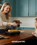 Woman using Ovente Two Serving Electric Indoor Grill And Panini Press Compact Contact Maker For Juicy Steaks Bold Smoky Flavor No Outdoor Mess Black Kitchen Appliance.