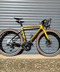 G24SL 1297g Carbon Gravel Wheelset For 700C with 40mm rim depth and 25mm inner width on yellow bike against a metal door.