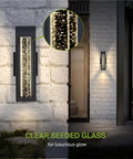 Lit Bubble Glass Tube Wall Sconce with Crystal Look illuminated on brick exterior at night, showing clear seeded glass glow