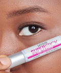 Woman holding 5 Day Extended Wear Strip Lash Adhesive With Brush Applicator near eye, clear formula, 4.8g bottle.