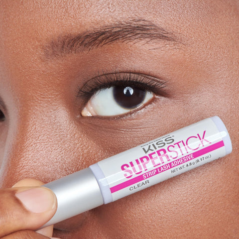 Woman holding 5 Day Extended Wear Strip Lash Adhesive With Brush Applicator near eye, clear formula, 4.8g bottle.