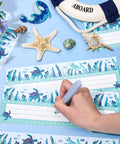 Person writing on 60 Pack Ocean Themed Sea Animal Name Tag Stickers For Back To School Marine Life Adhesive Labels, starfish nearby.