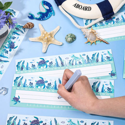 Person writing on 60 Pack Ocean Themed Sea Animal Name Tag Stickers For Back To School Marine Life Adhesive Labels, starfish nearby.