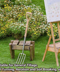 Beefy 4 Tine Garden Digging Fork With Long Ash Wood Handle And D Grip displayed on a wooden stand in a garden setting.
