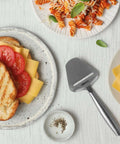 Stainless Steel Cheese Slicer Copenhagen Multifunctional Kitchen Tool beside grilled cheese sandwich and pasta on white tablecloth