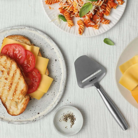 Stainless Steel Cheese Slicer Copenhagen Multifunctional Kitchen Tool beside grilled cheese sandwich and pasta on white tablecloth