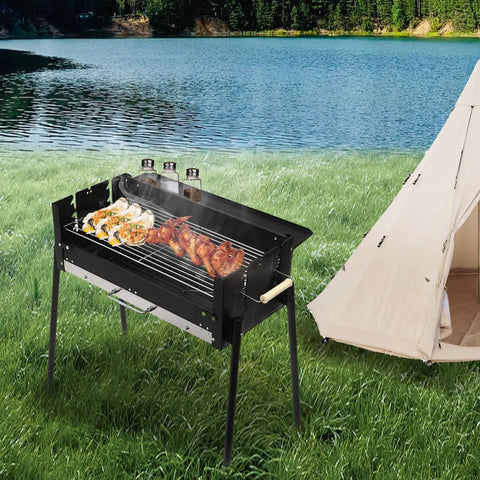Portable Charcoal Grill With Three Gear Height Adjustment for Three To Eight People in use by a lakeside campsite.