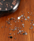 100 Piece Watch Screw Set With Micro Battery Clamp Screws, Stainless Steel Assortment for Watchmaking on wooden surface