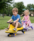 Two toddlers riding The Totally Hassle Free Wiggle Car For Toddlers With Super Slick Flashing LED Wheels on a park pathway.