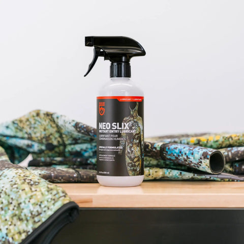 Neo Slix Wetsuit Entry Lubricant 16.9 Fl Oz bottle on table with colorful wetsuit, water based silicone free formula