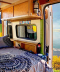 Cozy camper interior with "Happy Camper" sign above bed; Funny Camping Decor Sign For RV And Camper Interiors, Easy Install Wall Art.