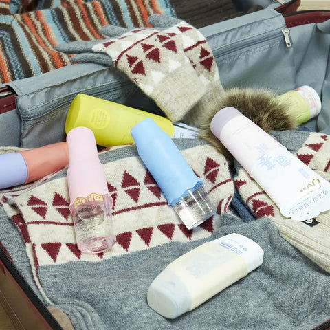 Silicone Bottle Covers 10 Pack for Travel Size Toiletries and Beach Vacay Essentials scattered in an open suitcase
