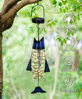 Handcrafted Iron Fish Lantern With Solar Powered Warm White LED Lights hanging in a garden, showing rustic nautical style.