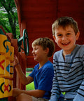 Smiling children playing with Tic Tac Toe Spinner Activity Panel for swing sets, backyard play accessory, durable UV protected plastic