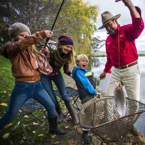 Family fishing by lake with Lightweight Folding Camping Stool Portable Chair Mini Foldable Seat For Adults Great For Fishing Hiking Gardening Beach With Carry Bag Camouflage Ideal For Campsites Picnics Fishing Trips And Outdoor Events visible.