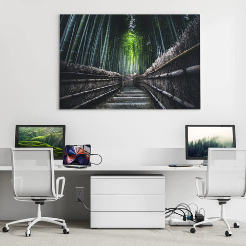 A minimalistic home office setup featuring two computers, a tablet, and a bamboo forest wall art backdrop.