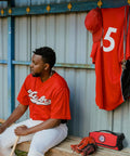 Side view of a red roll-up sports first aid kit with medical emblem, beside baseball gear in a dugout.