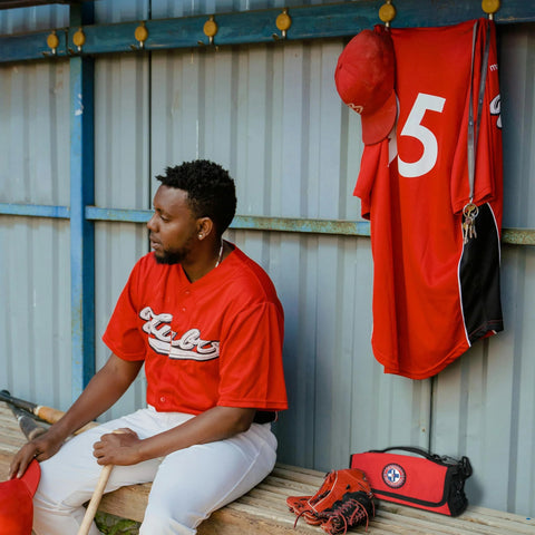 Side view of a red roll-up sports first aid kit with medical emblem, beside baseball gear in a dugout.